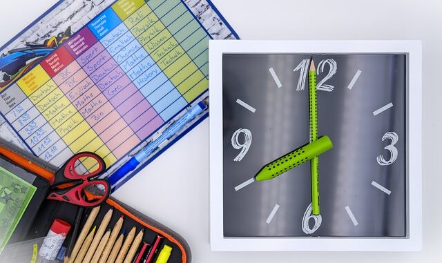 Grafika składa się z trzech części. W lewym dolnym rogu znajduje się czarny piórnik z czerwoną obwódką. W piórniku znajdują się, kredki, klej i nożyczki. W lewym górnym rogu znajduje się kolumnowy plan lekcji. Każdy dzień zaznaczony jest innym kolorem. Po prawej stronie znajduje się zegar ścienny. Wskazówki zegara są zielone, tarcza zegara jest w kolorze szarej z białymi cyframi.