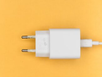 Na żółtym tle znajduję się biała ładowarka do sprzętu elektronicznego.